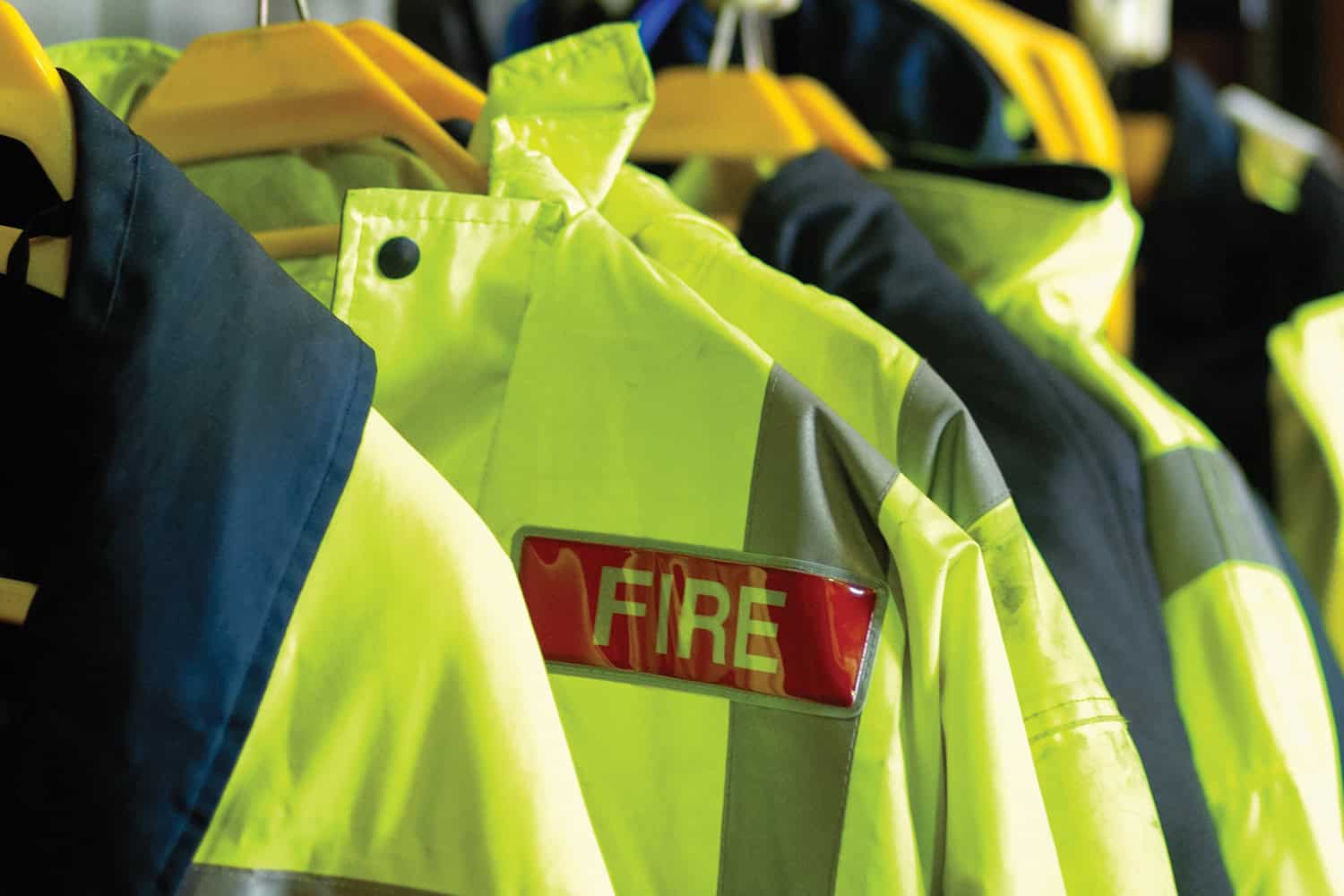 Photo of firefighter’s helmet sitting on a shelf above a rack of high-vis jackets.