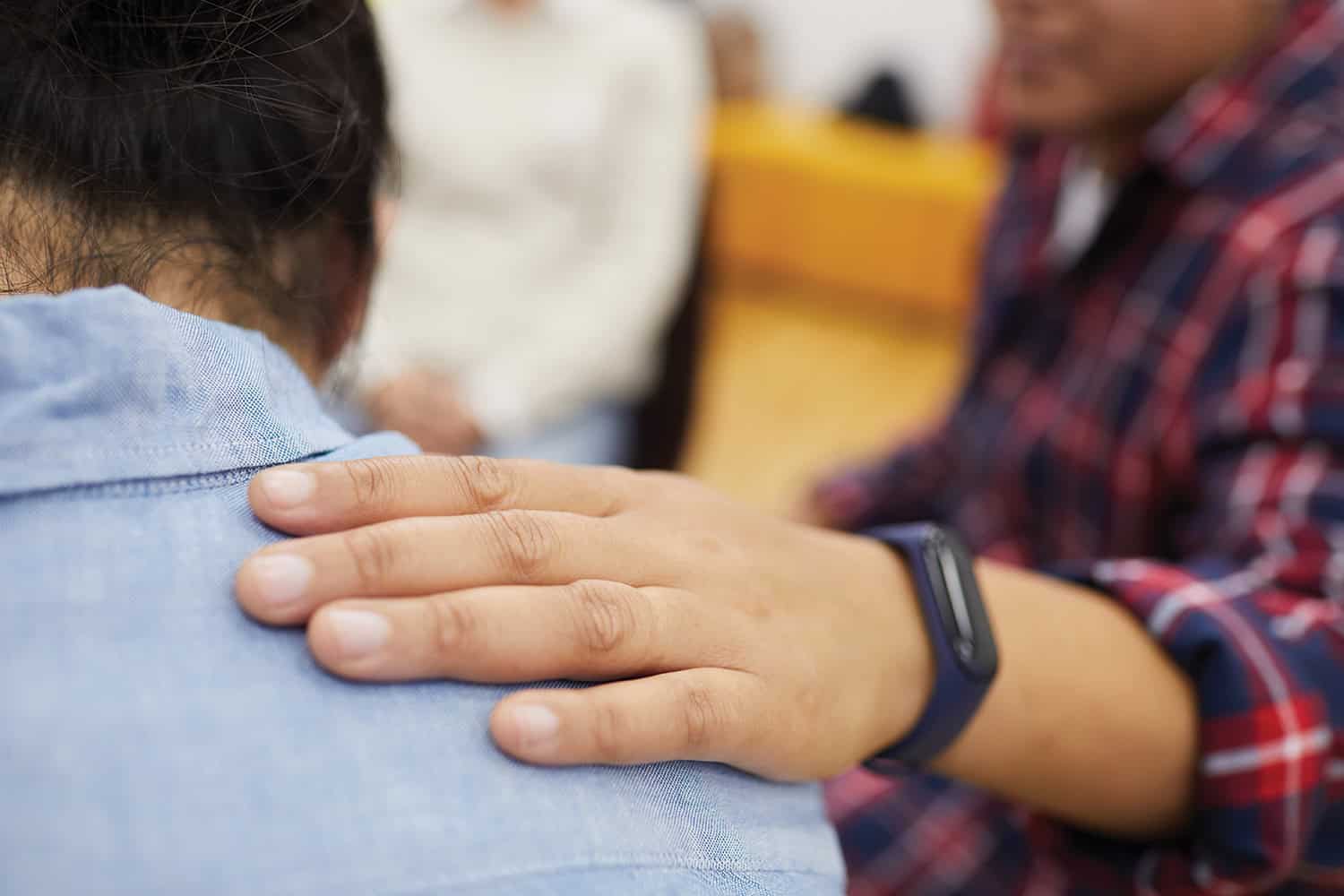 close-up of someone’s hand resting on another’s shoulder, comfortingly, during a group therapy session
