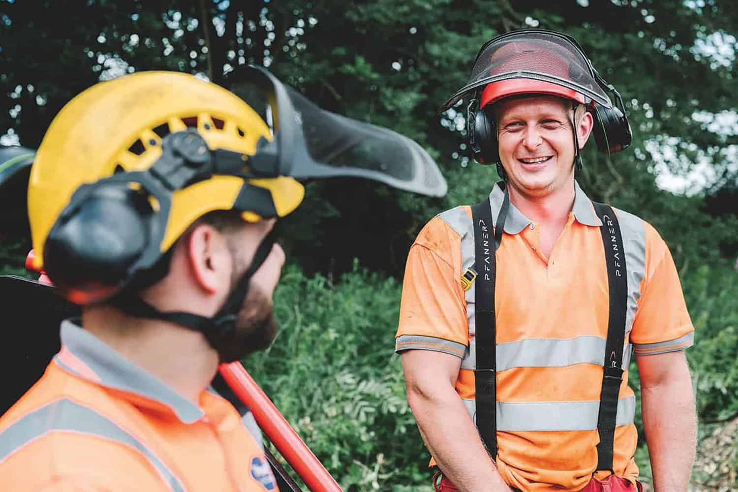 photo of arborists in orange workshirts, helmets with face shields and ear protectors; photo of local government national recruitment campaign poster on side of bus stop next to busy urban road with blurred bus going past in the rain