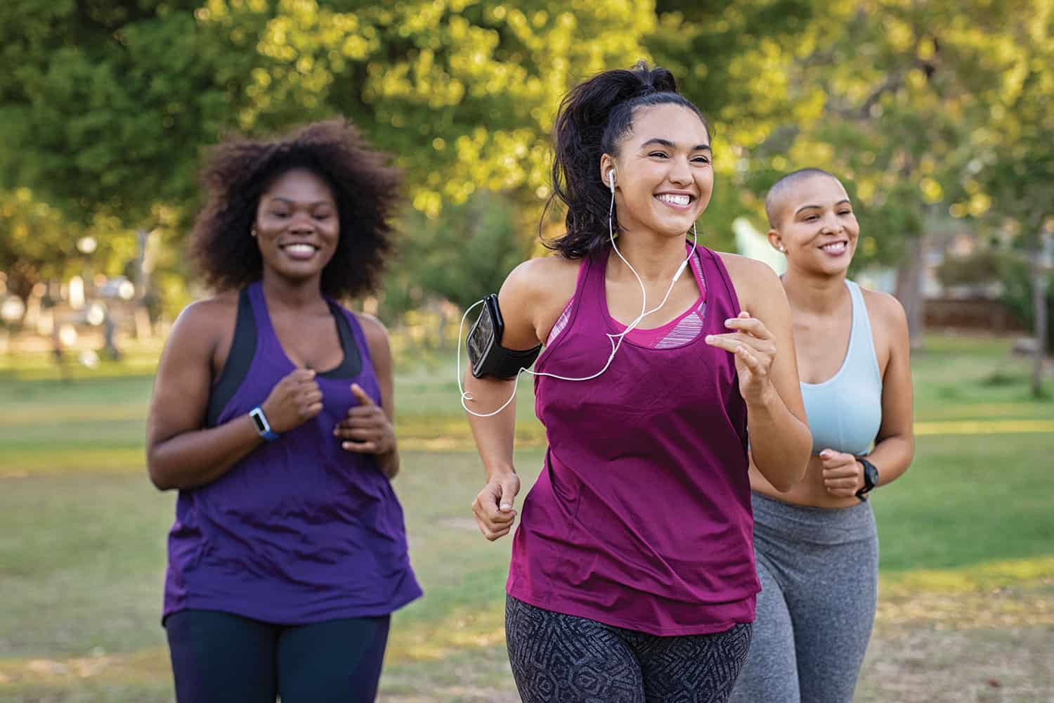 photo of three women of different ethnicities smiling and running in a park