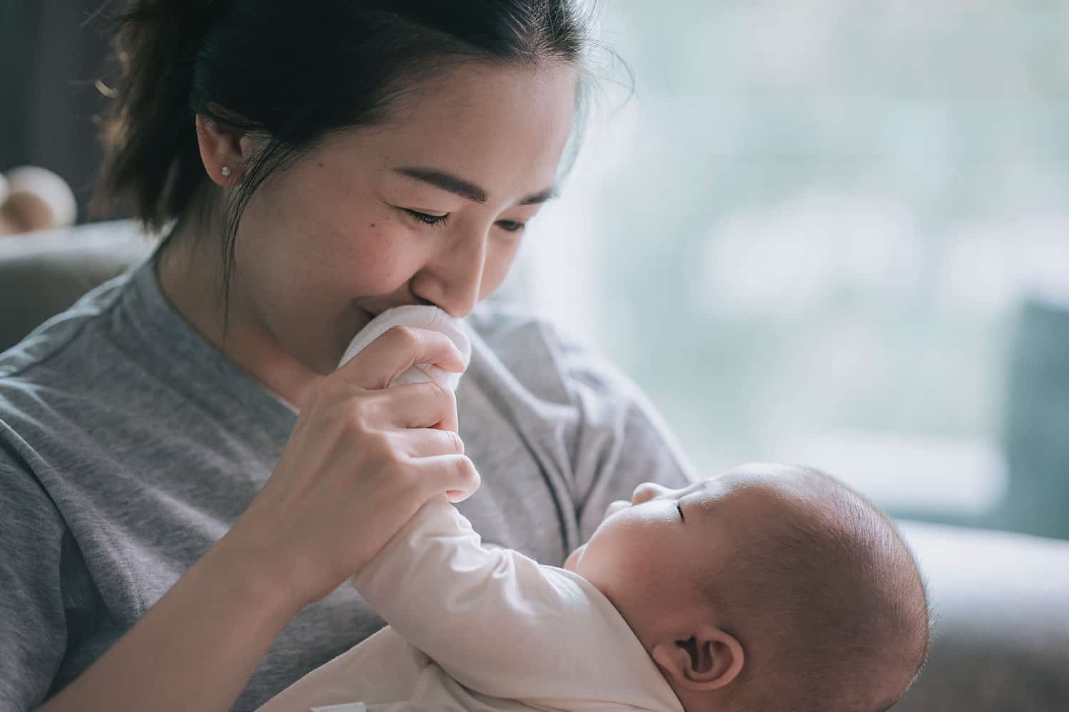 photo of mother holding and looking at her baby and holding its hand to her mouth to kiss