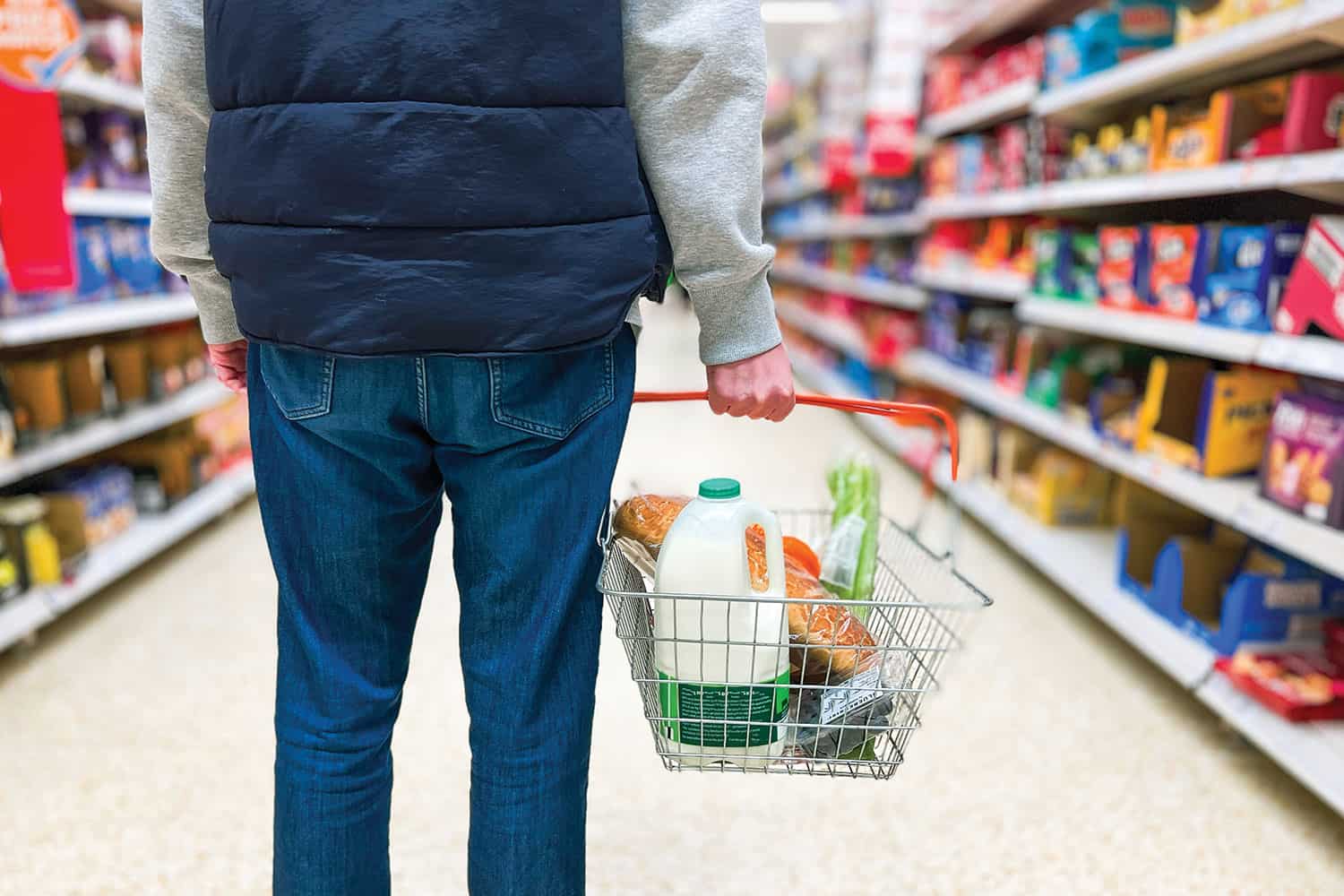 photo from behind of casually dressed male shopper holding shopping basked standing in ailse of a supermarket