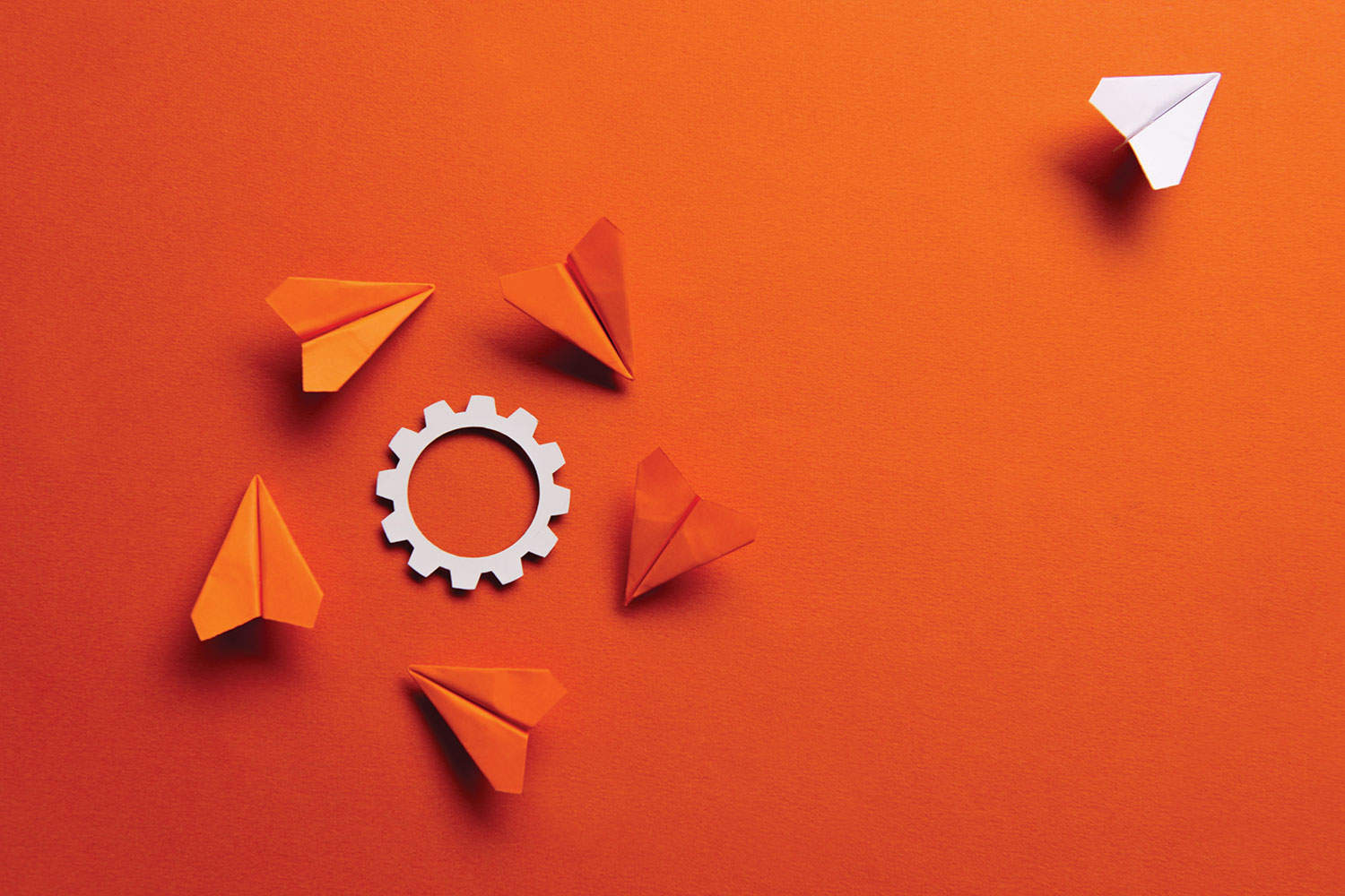 graphic of orange paper planes circling a white cog on an orange background, with one white aeroplane flying out of the frame at the top right-hand corner.