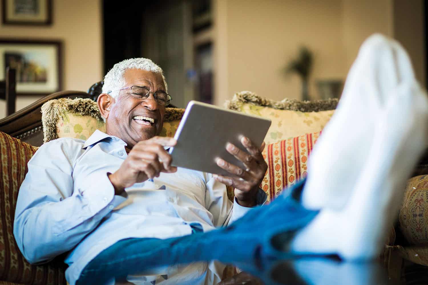 photo of older man on sofa with feet up smiling at tablet