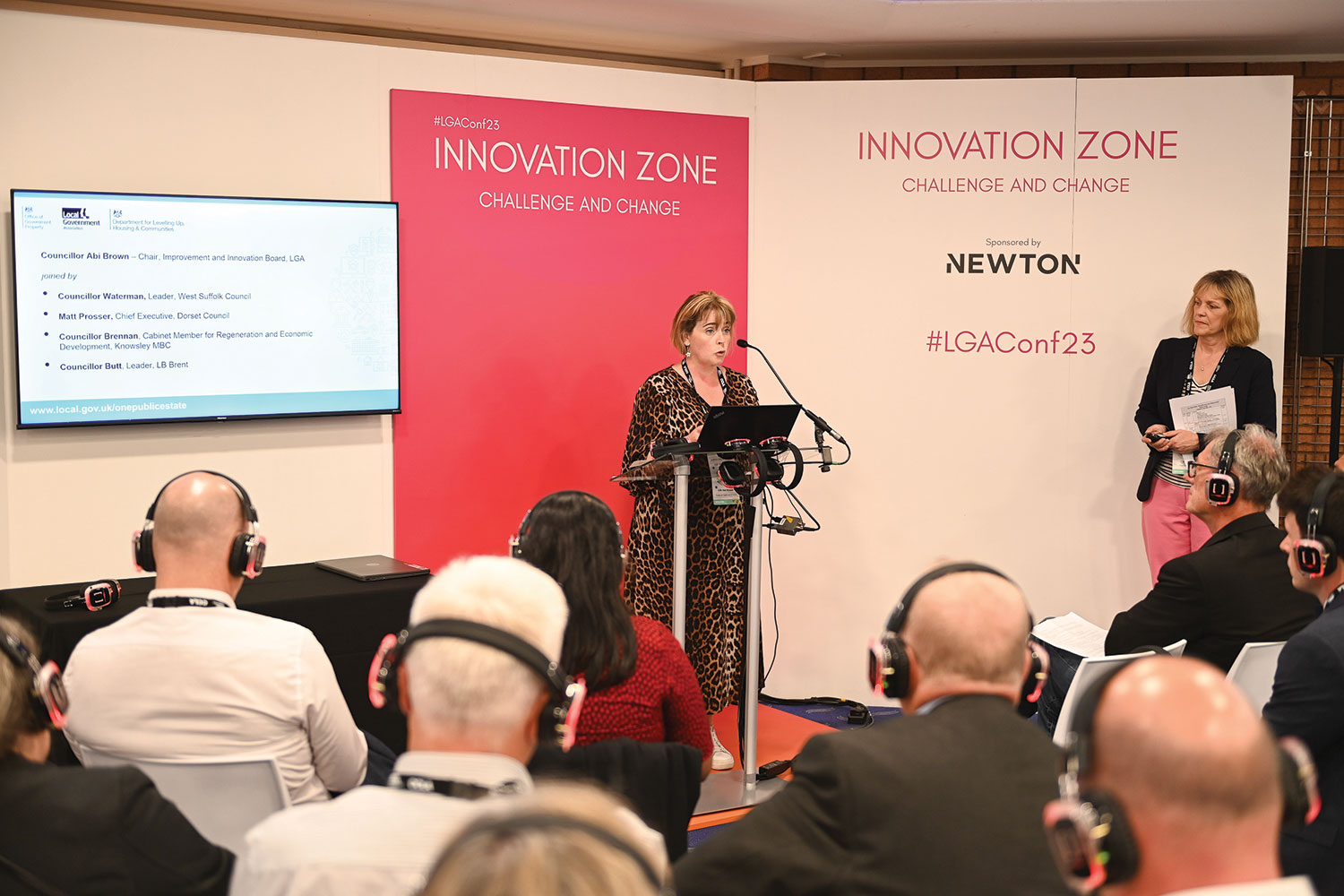 view from behind seated delegates wearing headphones of Cllr Abi Brown OBE, Chairman of the LGA’s Improvement and Innovation Board, speaking in the Innovation Zone at the LGA’s 2023 annual conference in Bournemouth;