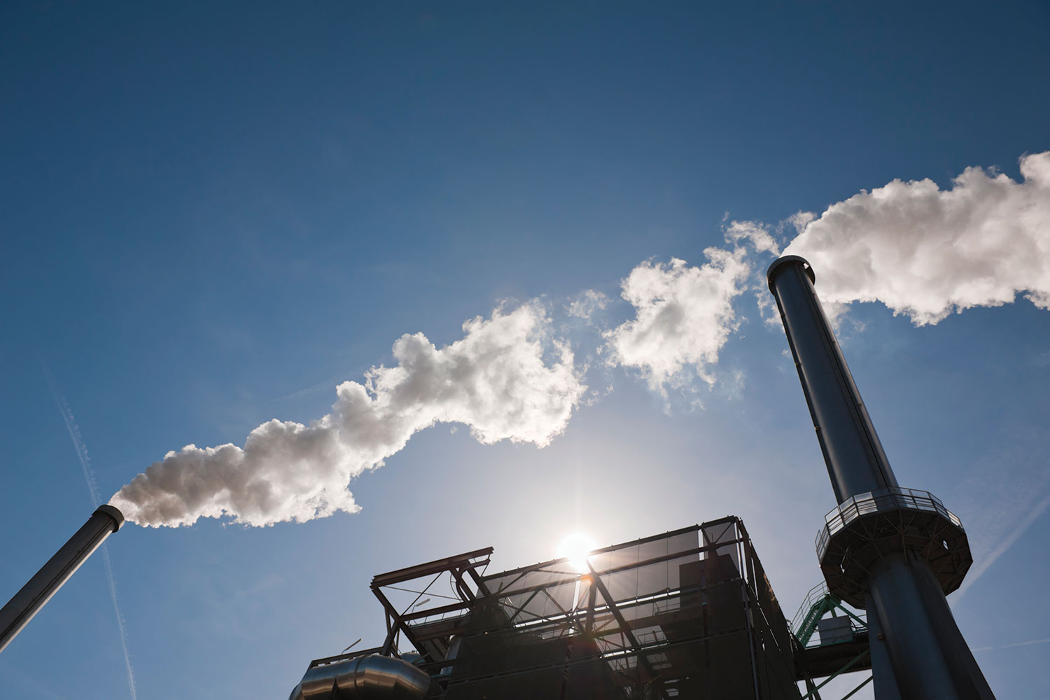 photo of industrial chimneys belching smoke into a blue sky