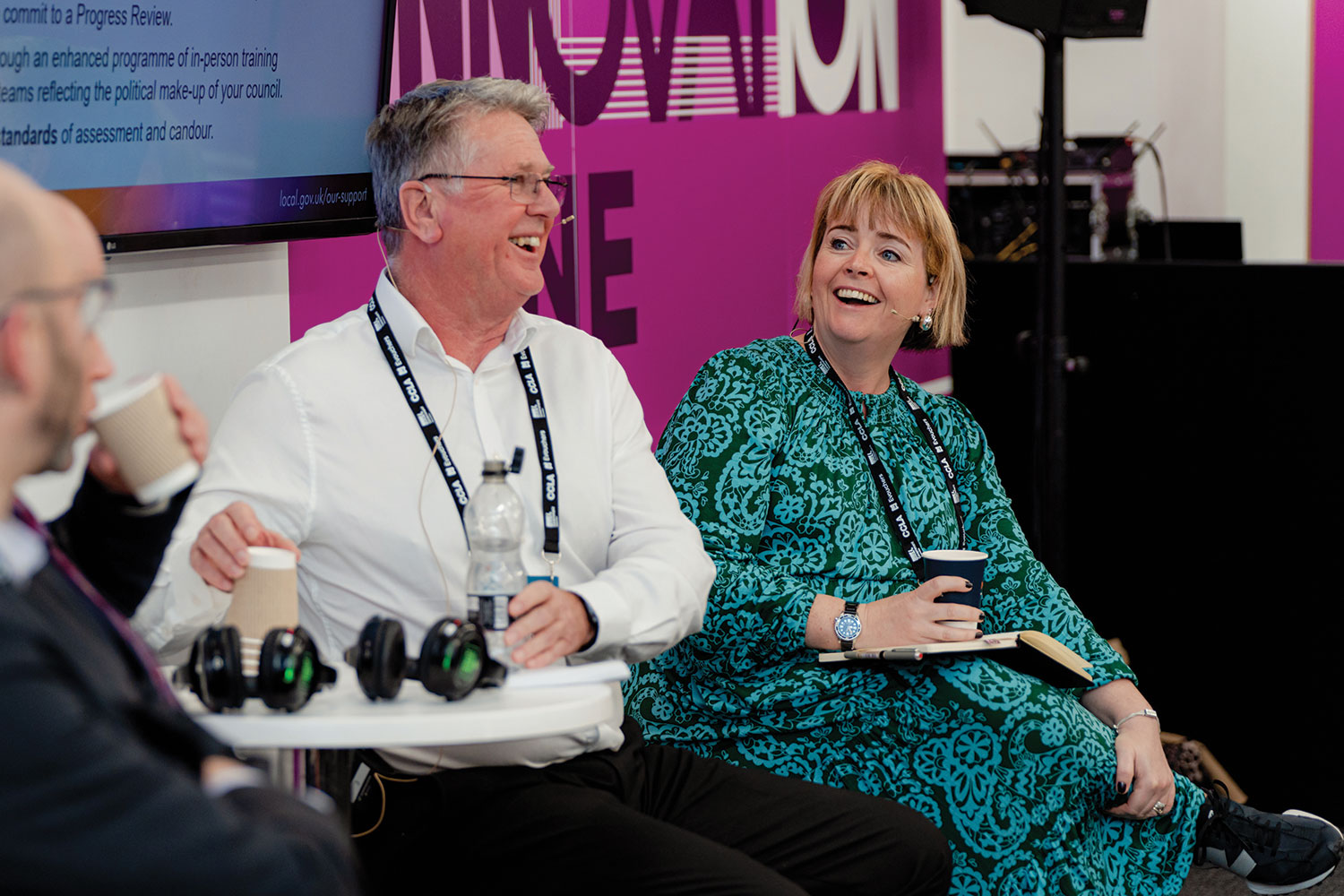 photo of Cllr Abi Brown MBE, Chairman of the LGA’s Improvement and Innovation Board, laughing with Gavin Jones, Leader Commissioner for Slough Borough Council, both sitting with Innovation Zone sign behind them and drinks in hands