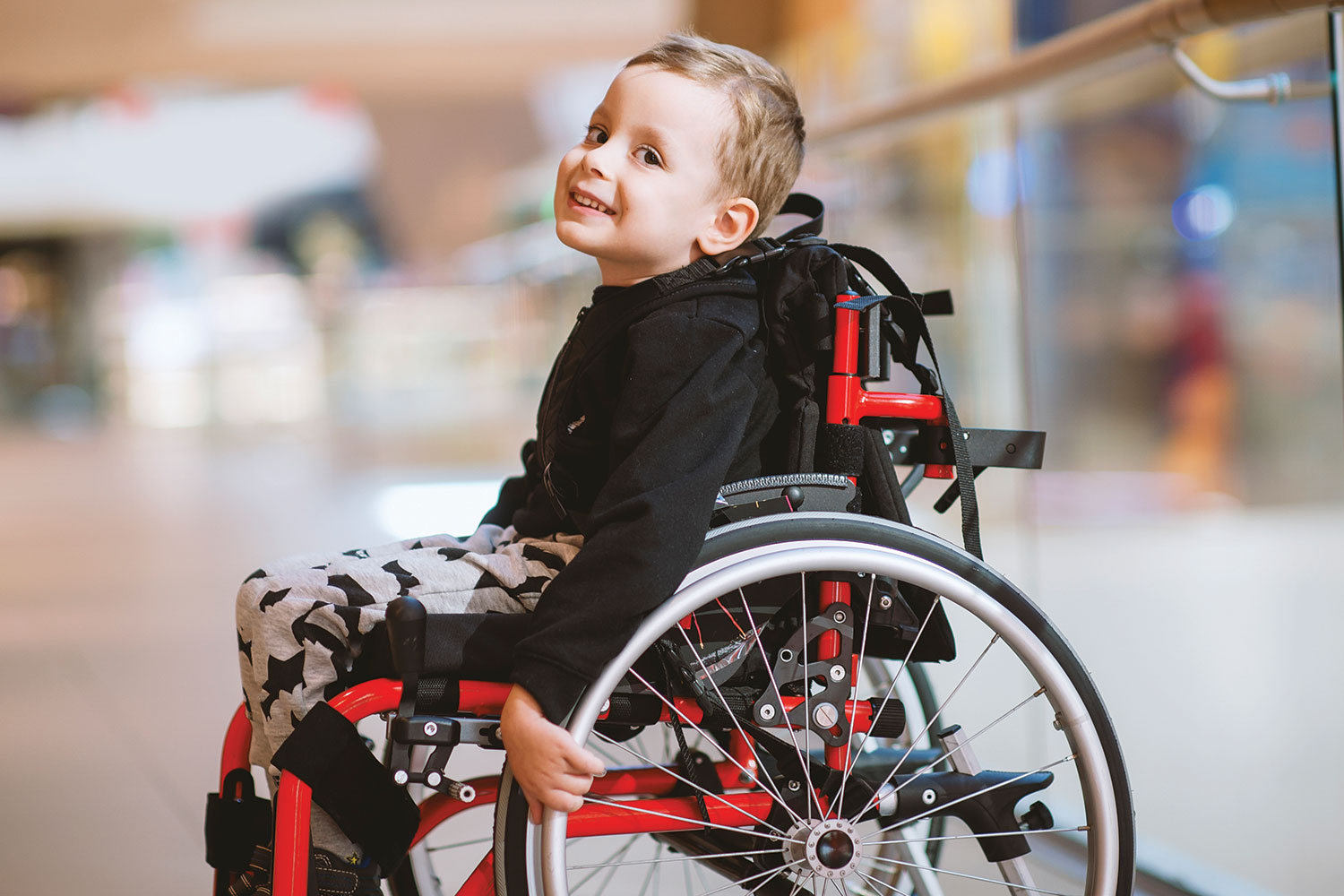 : photo of smiling young disabled boy in red and black wheelchair