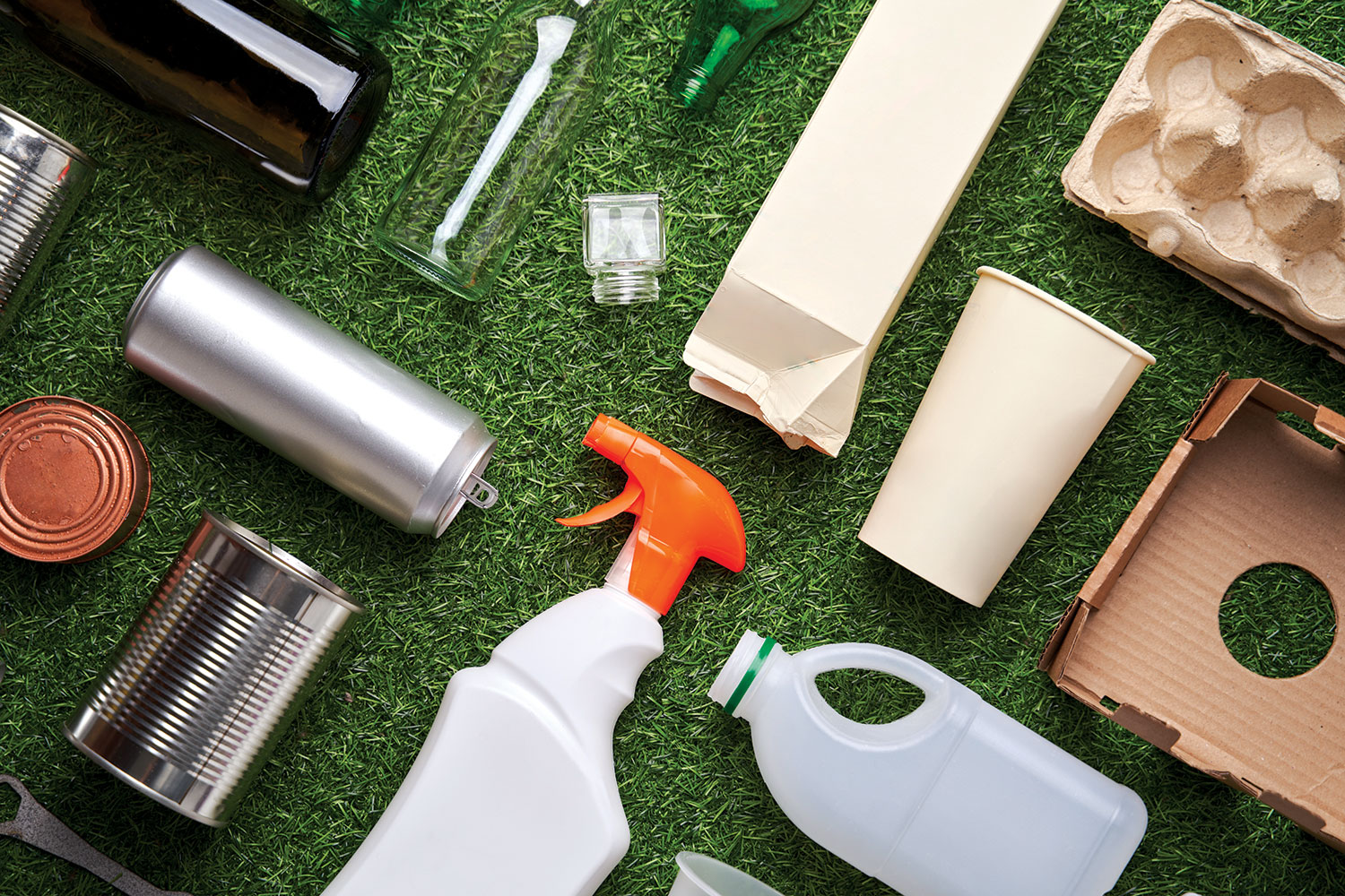 photo of clean individual pieces of packaging – tin cans, glass and plastic bottles, egg box and other cardboard packaging – laid out symmetrically on grassy background