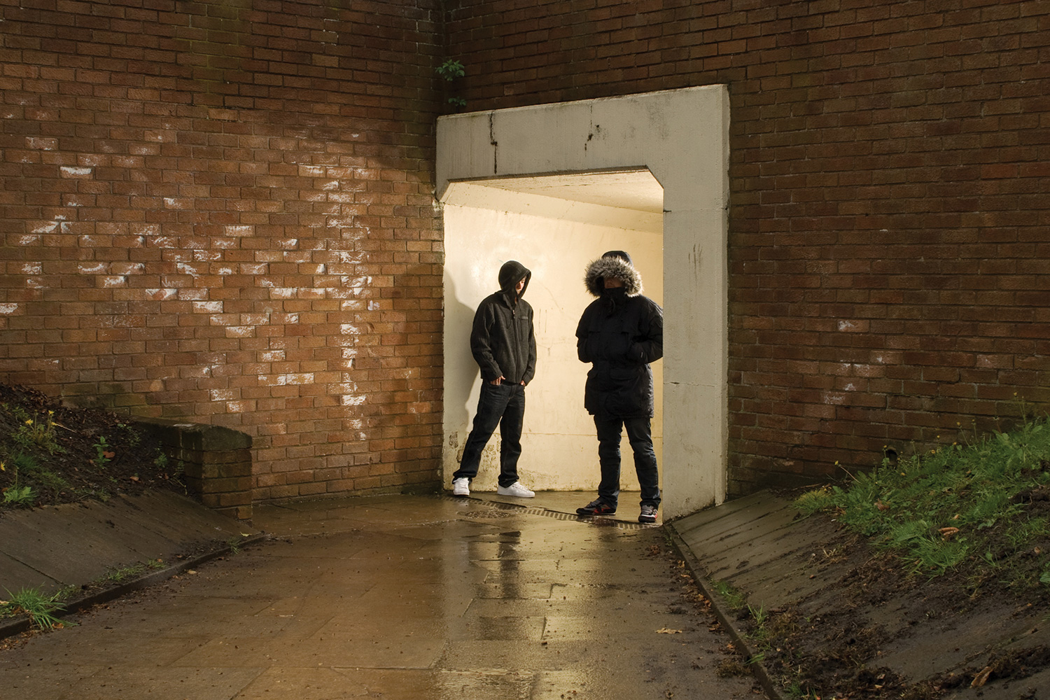 Two young men in hoodies hanging around entrance to subway at night.