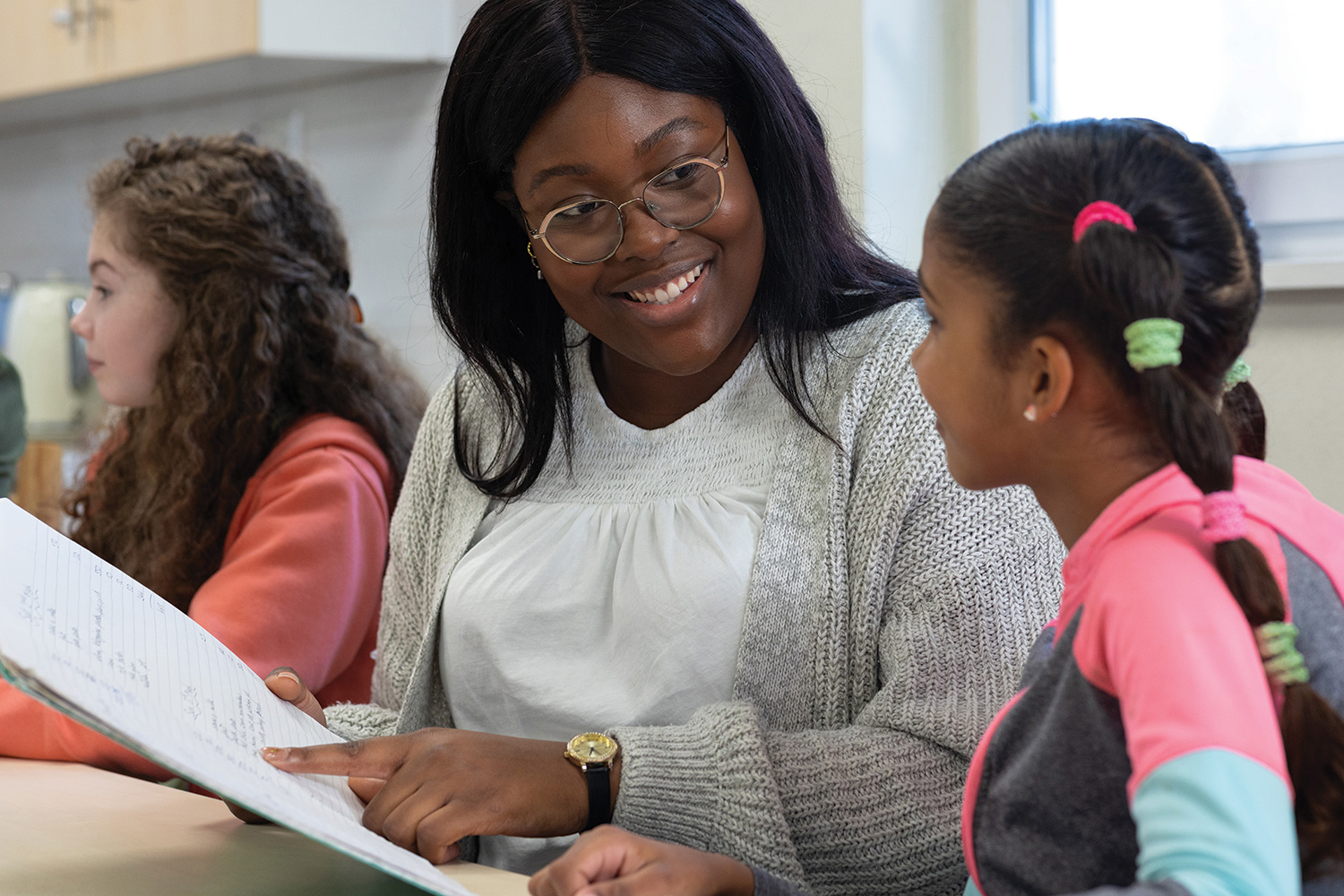 Woman social worker pointing to a book and smiling at young girl.