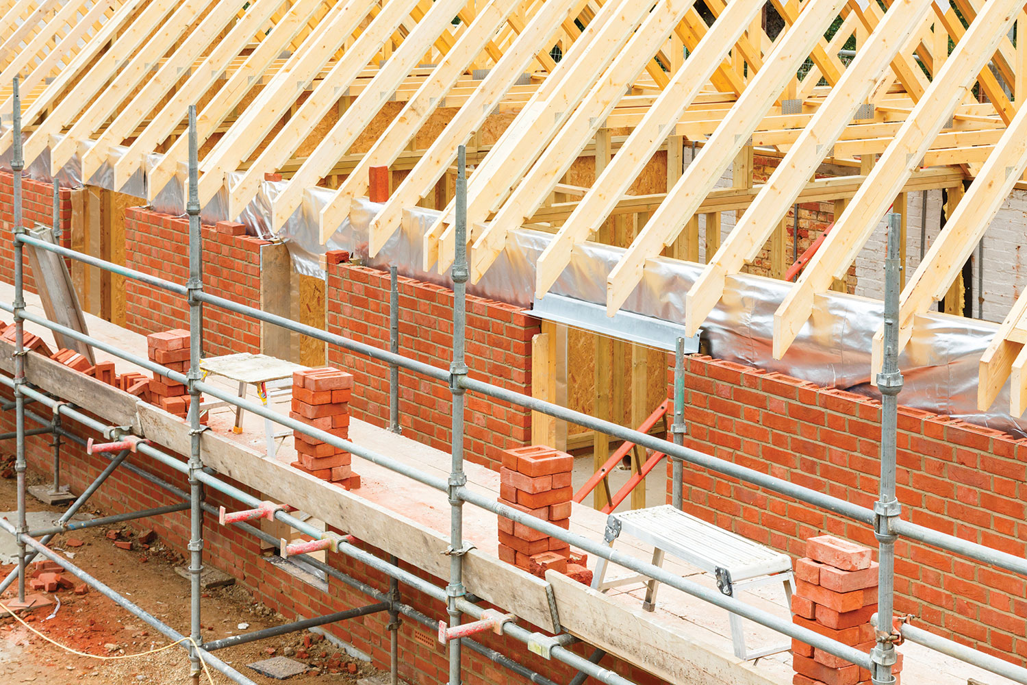 Close-up of new block of homes being built, with scaffolding alongside red brick walls and wooden roof beams,