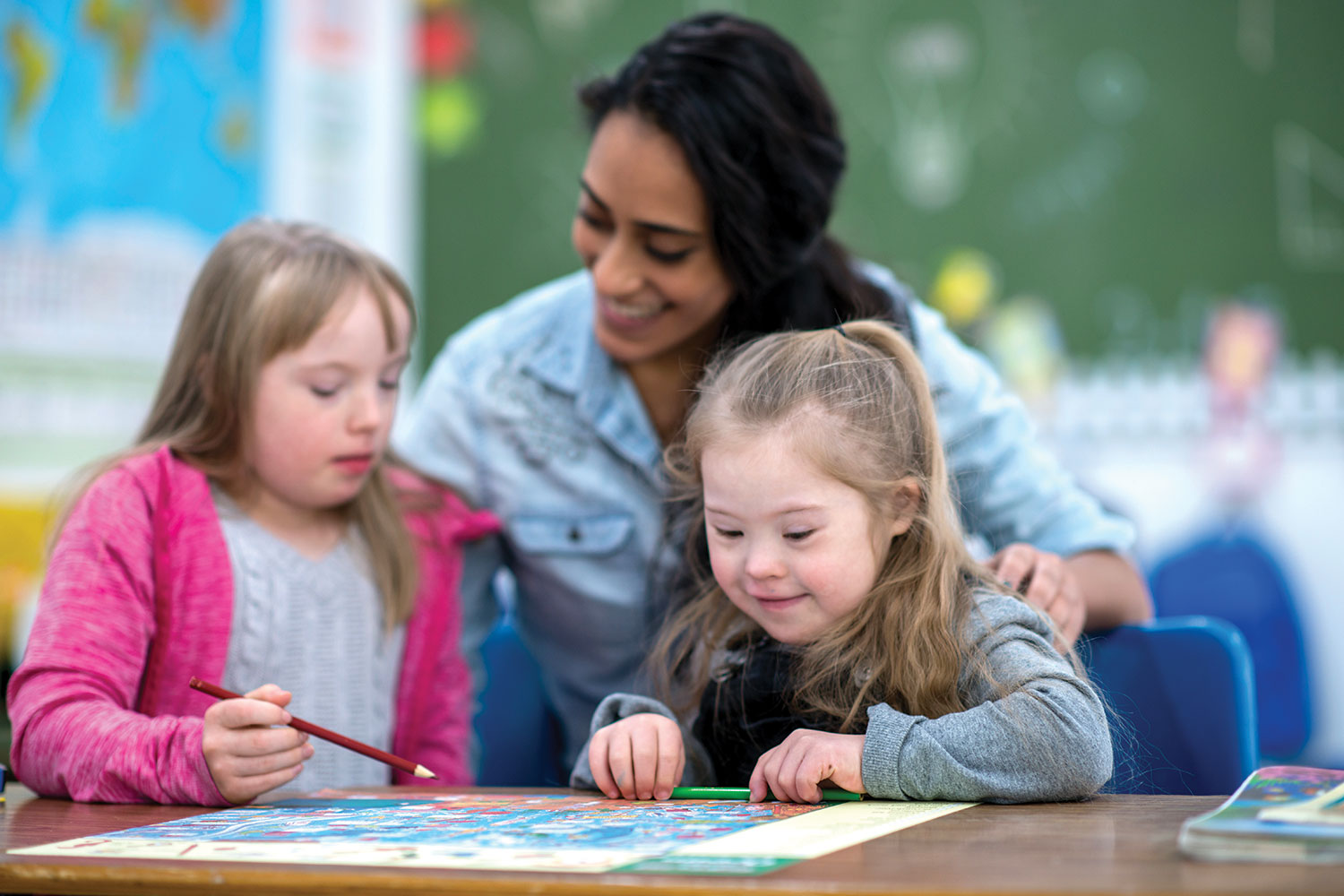 female teacher working with two young girls in classroom, one with Down Syndrome