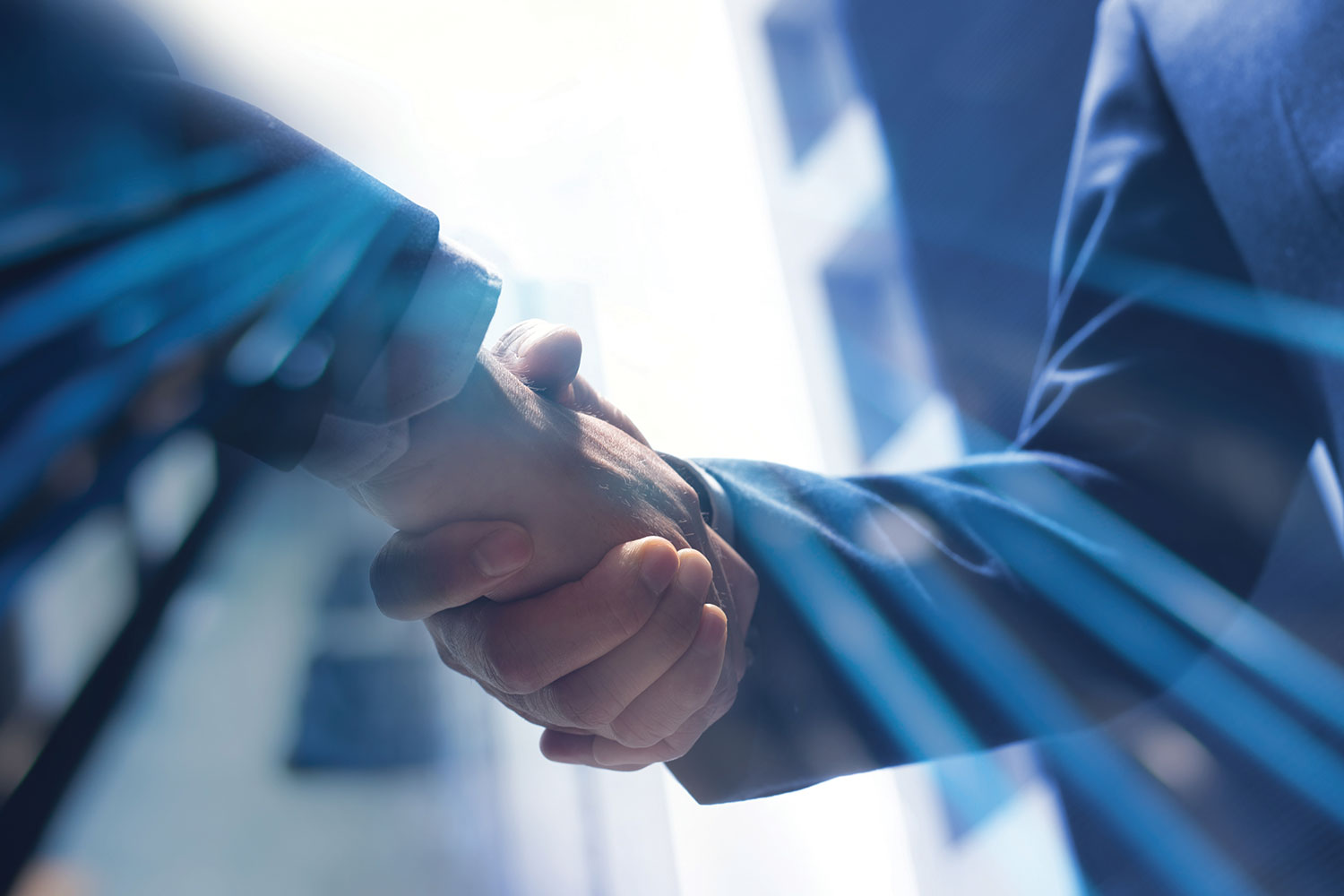 close-up of two people shaking hands with light defracted around the handshake and blurred buildings in the background