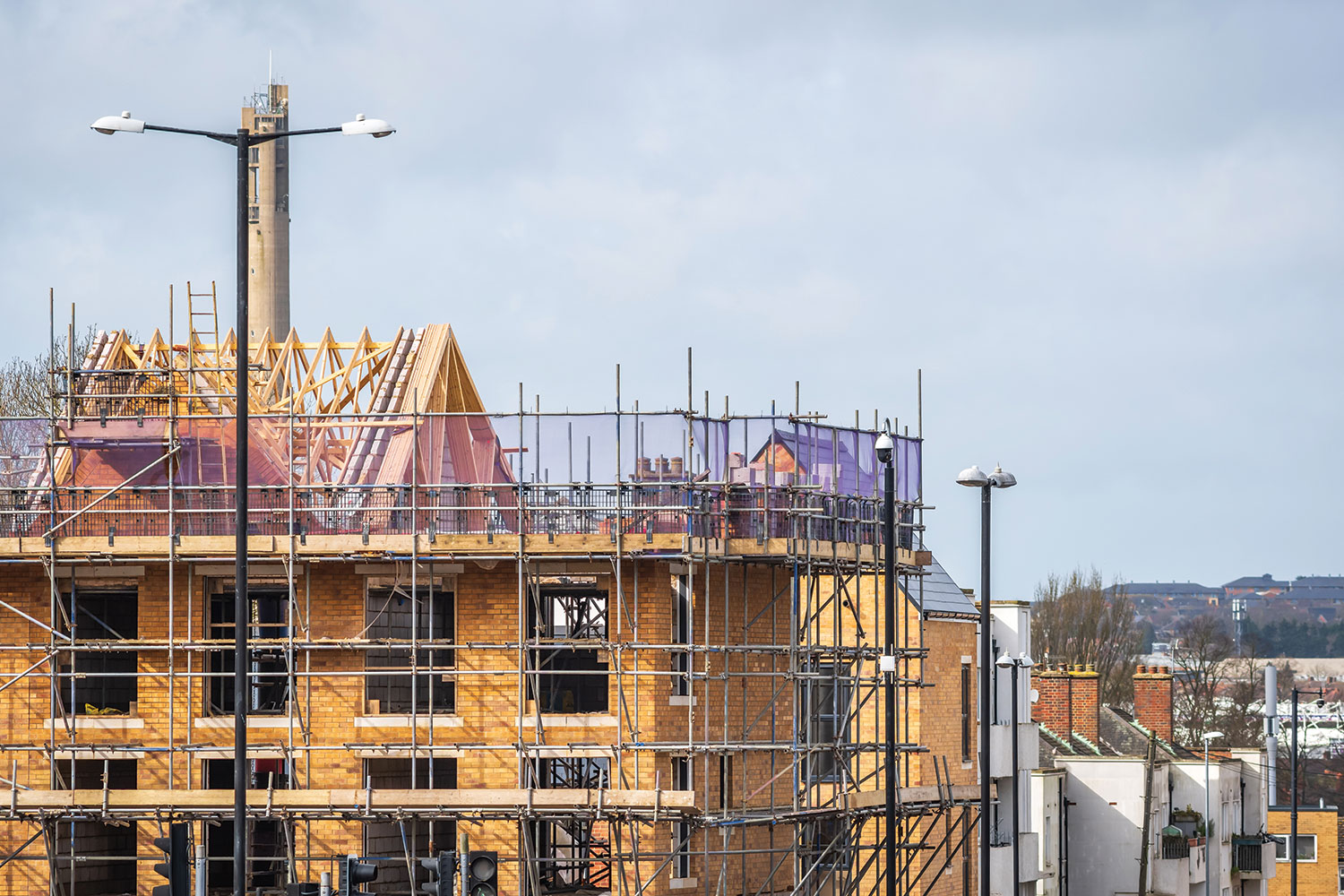 photo of new housing going up, surrounded by scaffolding, at end of an established residential street, dropping downhill into the background