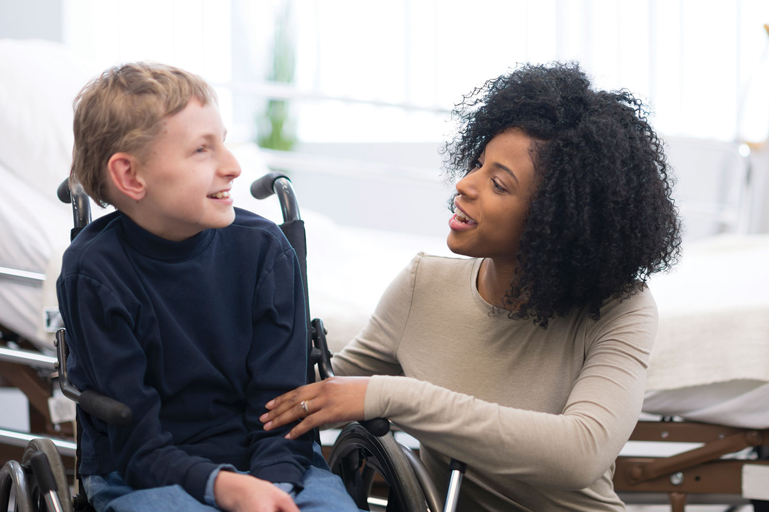 photos of woman carer kneeling beside young disabled boy in wheelchair, and middle-aged female carer and older woman sitting on a sofa