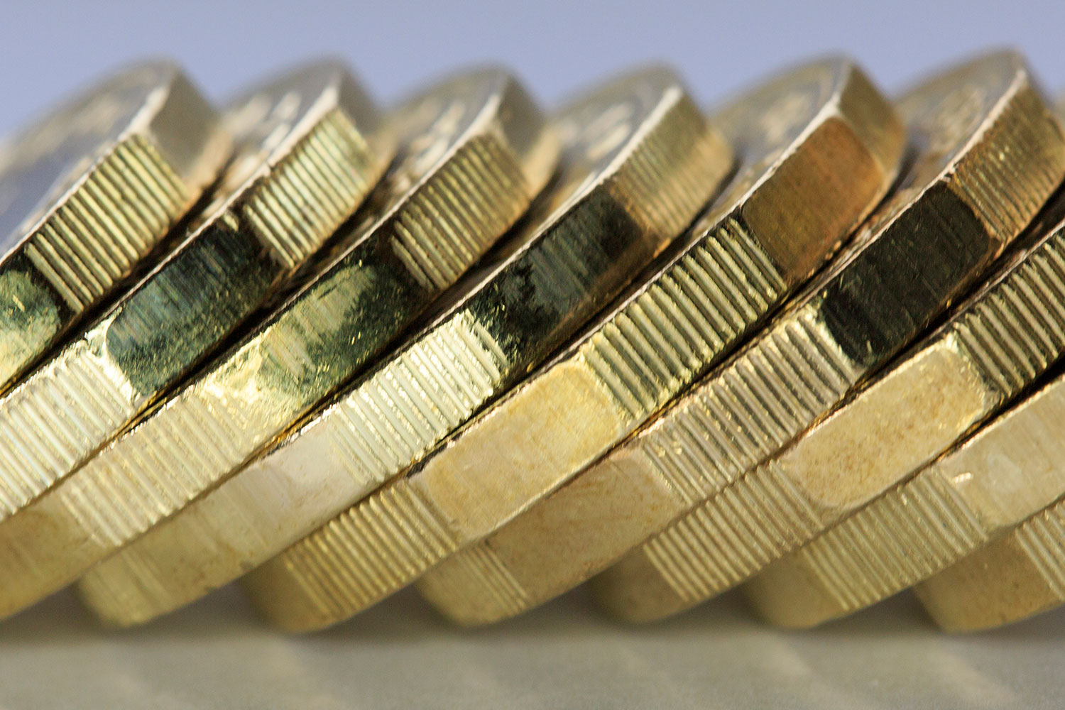 close-up photo of edges of golden UK pound coins leaning to the right against each other