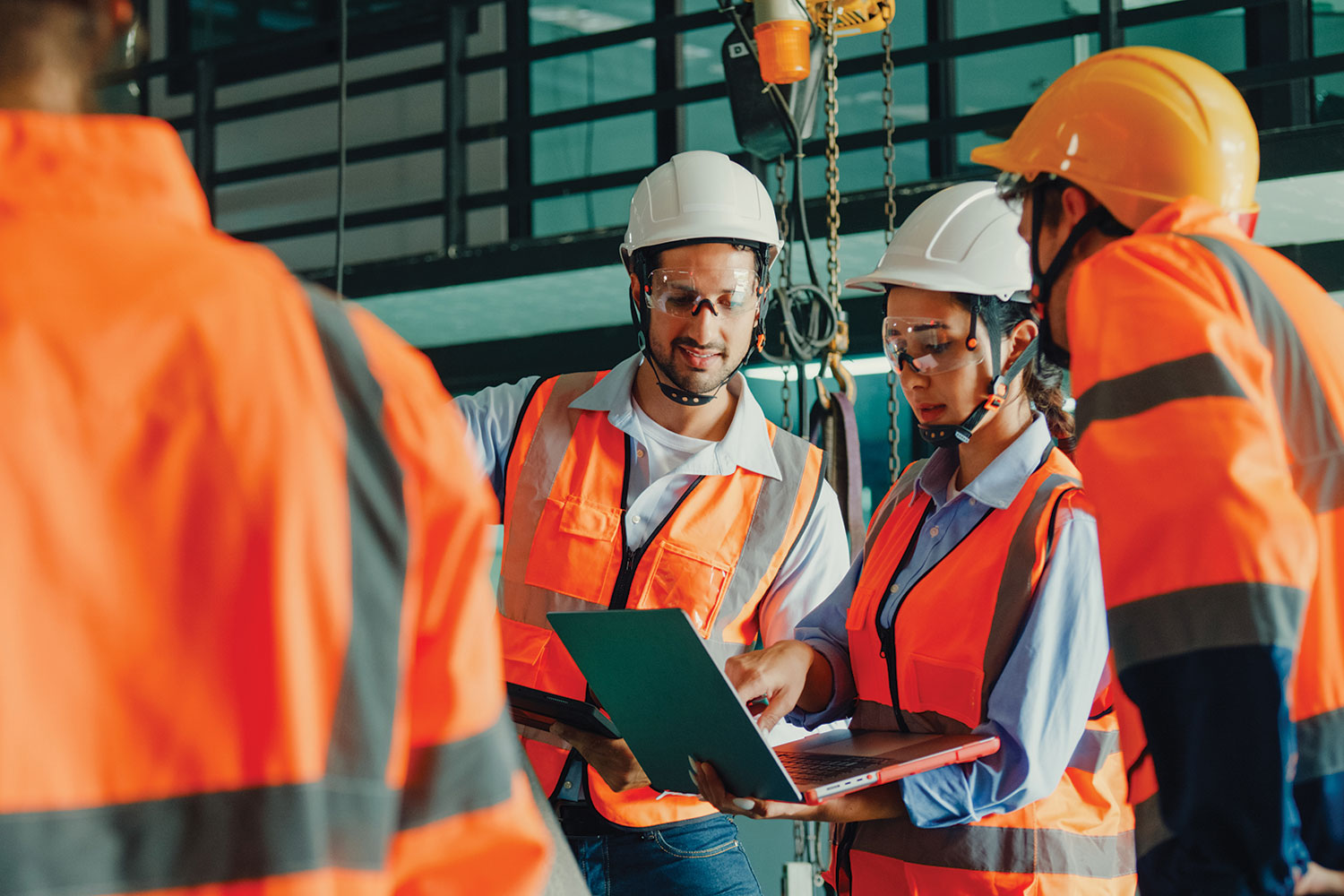 photo of group of apprentices in hard hats and high-vis orange jackets looking at laptop in factory setting