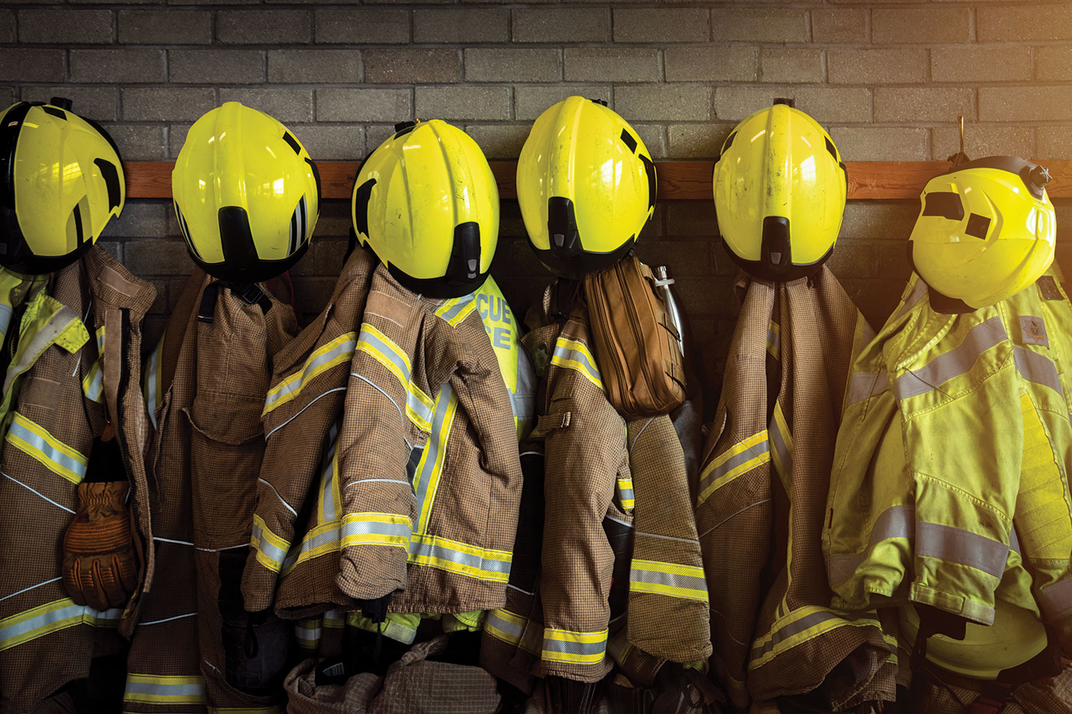 of fire jackets and yellow fire helmets hanging on an internal brick wall